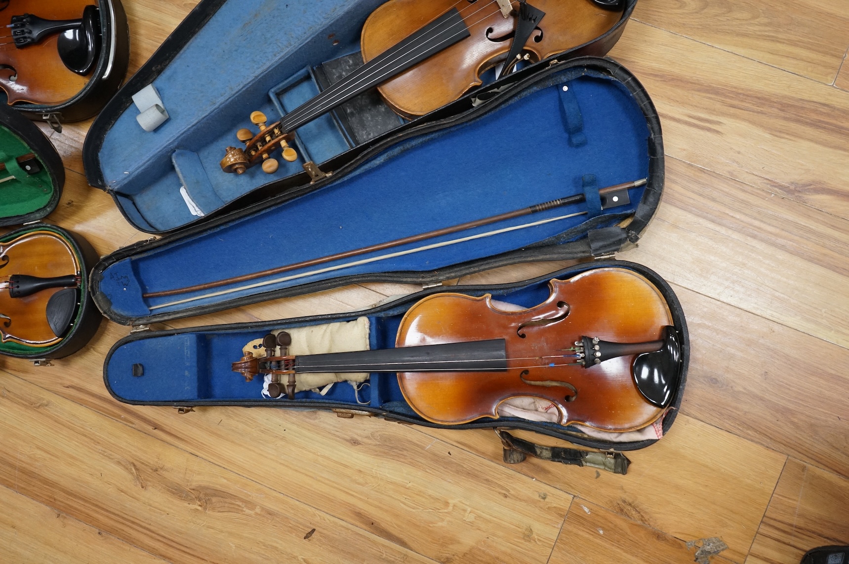 Five cased 20th century violins, including; a German violin, two Czech violins, a three-quarter size violin with a label for Bienfait, and a Romanian quarter size violin, all in cases or the remains of cases.